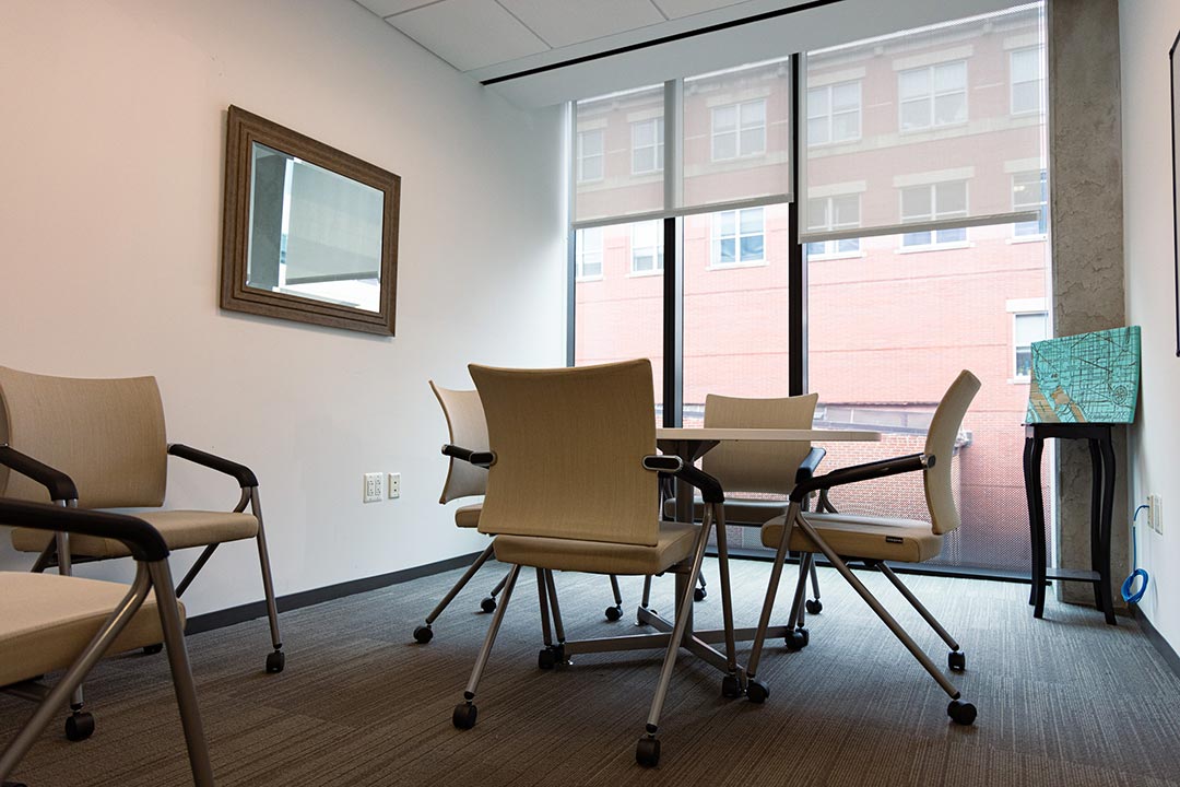 Chairs set up around a table in a well-lit room with a wall of windows
